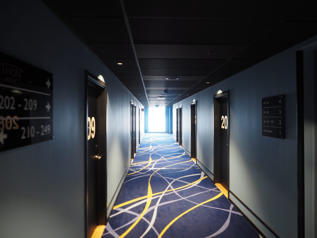 Langer Hotelflur mit Zimmertüren und regelmäßig angeordneten Deckenleuchten.