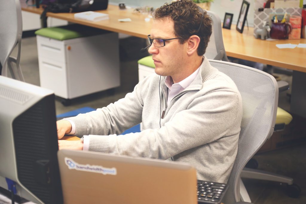 Schreibtisch mit Computer in einem offenen Büro- und Coworking-Bereich.