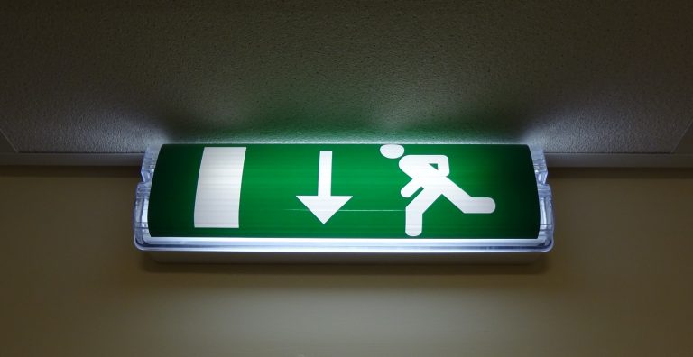 Grün leuchtendes Rettungszeichen mit laufender Person und Richtungspfeil.