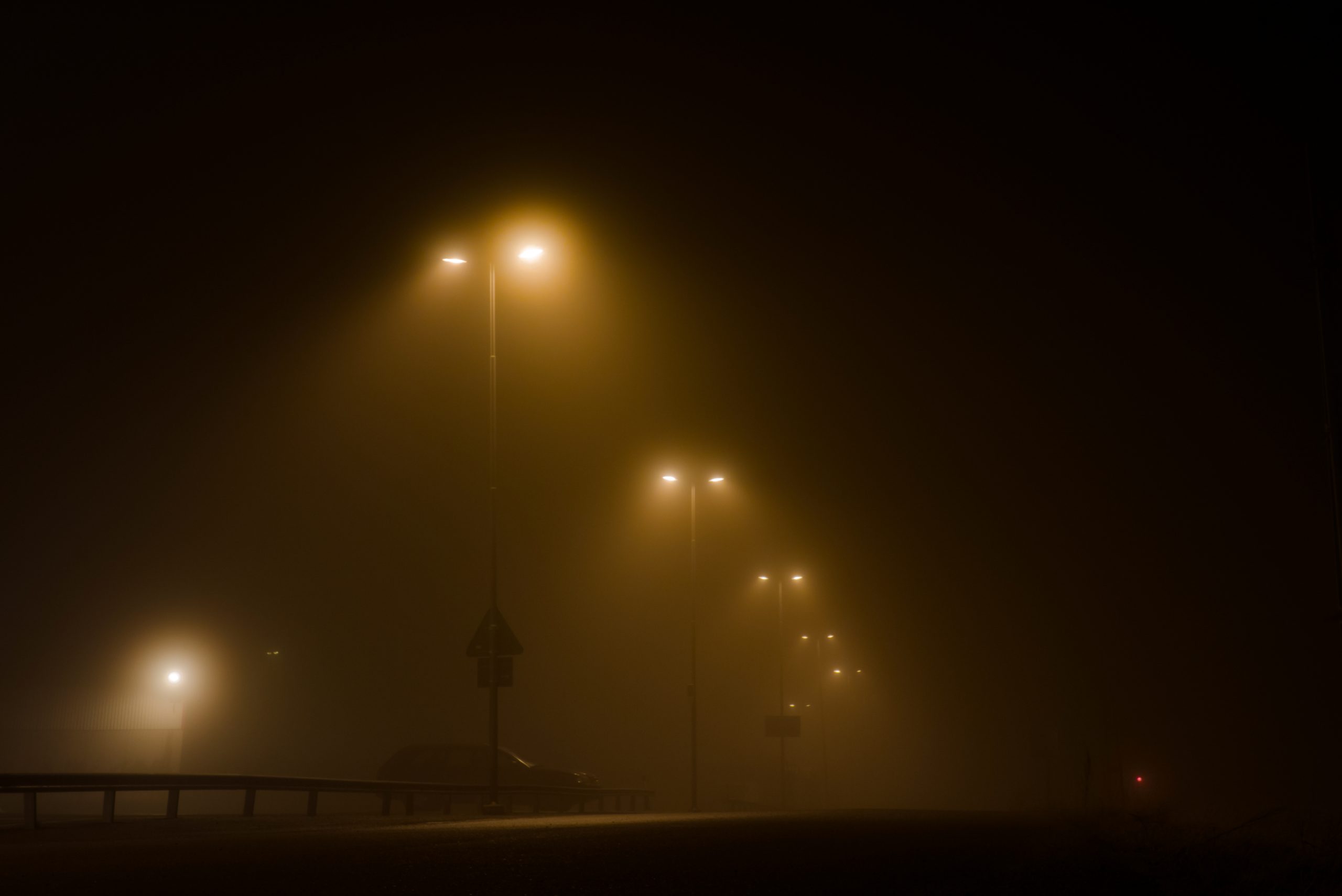 Parkplatz bei Nacht mit mehreren leuchtenden Masten, Fahrzeugen und leichtem Nebel.