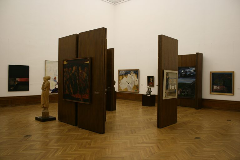 Galerieraum mit einzeln beleuchteten Gemälden und Skulpturen