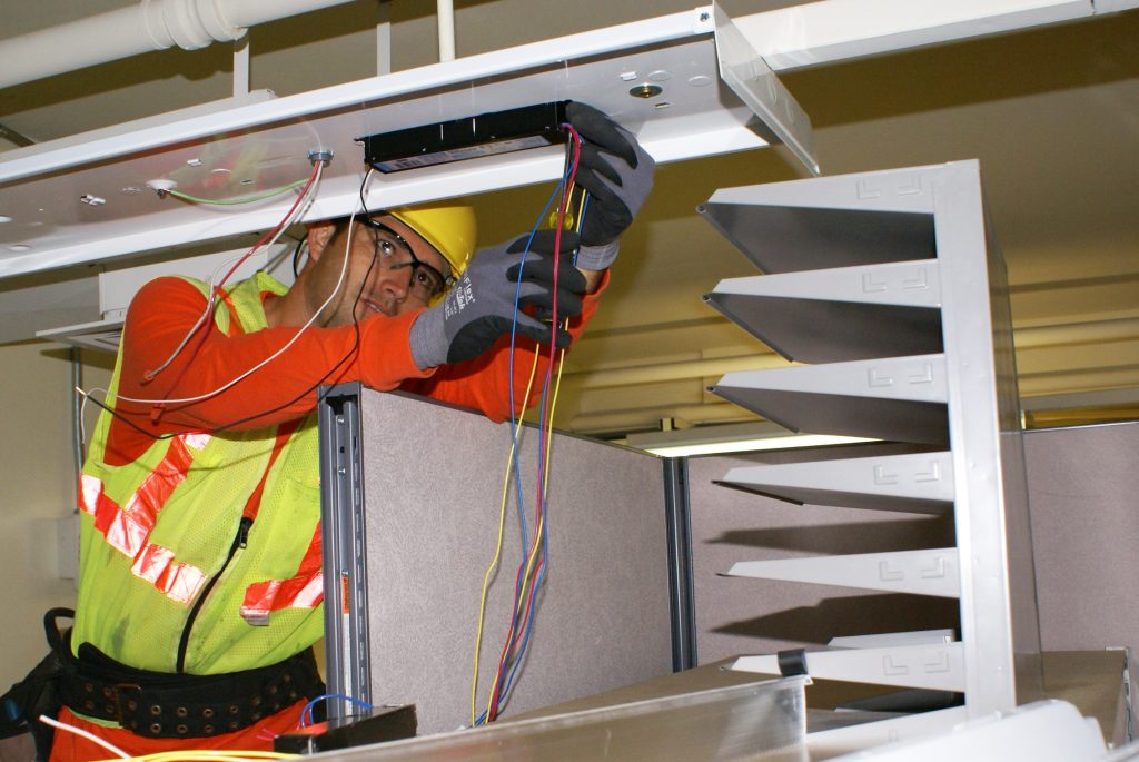 Elektriker arbeitet an der Neuverdrahtung einer Deckenleuchte für ein Beleuchtungs-Retrofit.