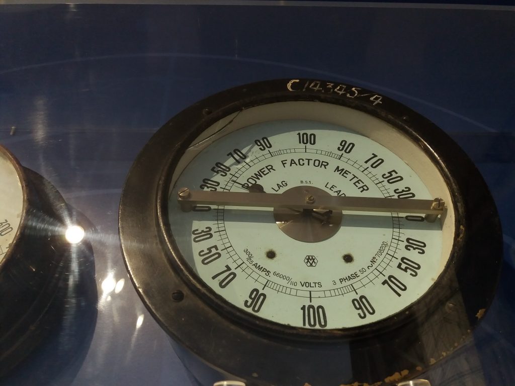 Analoges Leistungsfaktormessgerät an einer historischen elektrischen Schalttafel.