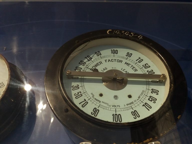 Analoges Leistungsfaktormessgerät an einer historischen elektrischen Schalttafel.