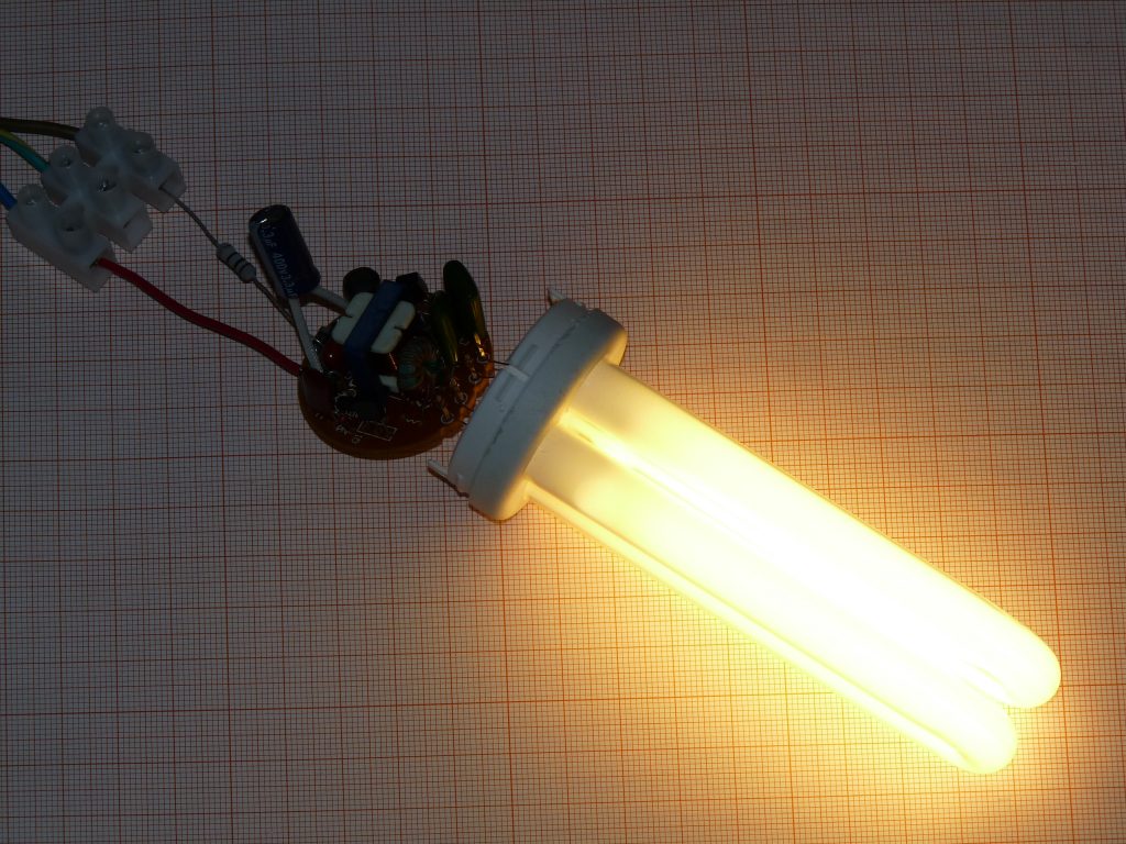 Leuchtende Kompaktleuchtstofflampe an einem geöffneten älteren Vorschaltgerät.