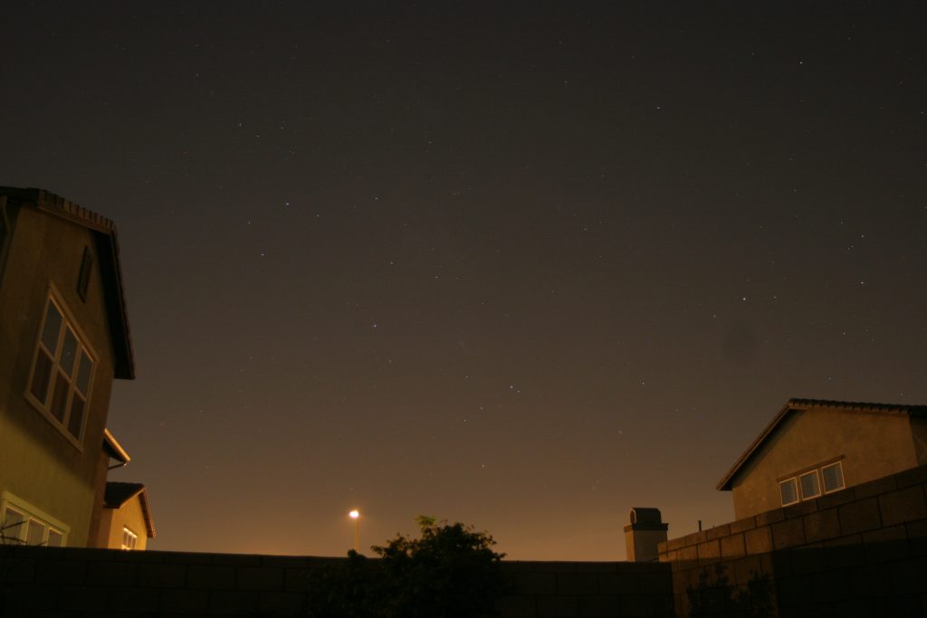 Nächtlicher Himmel über einem Vorort mit sichtbarer Aufhellung, Blendung und seitlich einfallendem Licht.