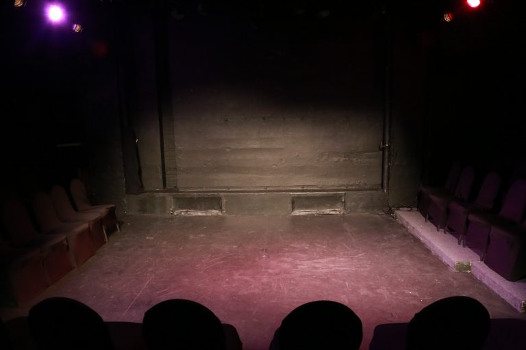 Leere schwarze Theaterbühne mit mehreren sichtbaren Lichtkegeln auf dem Boden