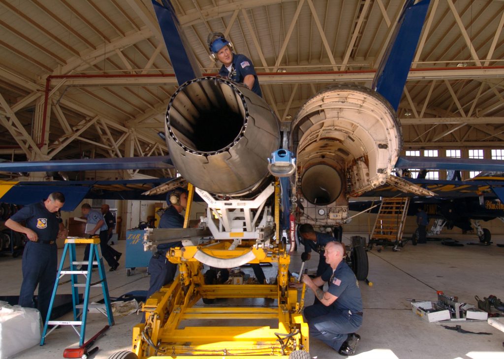 Techniker warten ein Flugzeug in einer hohen, gleichmäßig beleuchteten Wartungshalle.